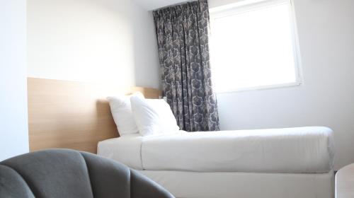 a white couch in a room with a window at Geographotel Paris-Roissy CDG Airport in Le Mesnil-Amelot