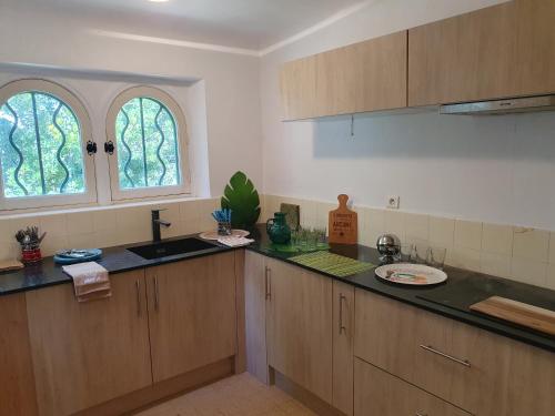 - une cuisine avec des placards en bois, un évier et 2 fenêtres dans l'établissement Charmante Villa Provençale pieds dans l'eau avec piscine et plage privée, à Saint-Raphaël