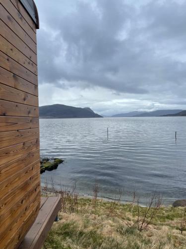 a wooden building next to a body of water at Sleeping barrel lodge Smaken av Ryfylke Event AS, drives ikke som hotell in Hjelmeland