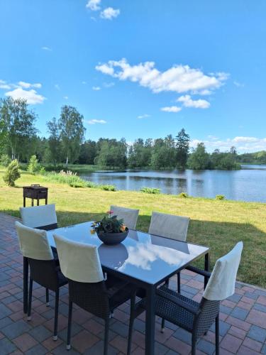 a table and chairs on a patio next to a lake at Viesu nams ADLERI in Saldus