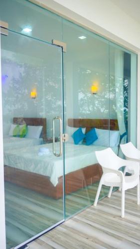 a glass room with a bed and a white chair at Dinuda Resort in Kalpitiya