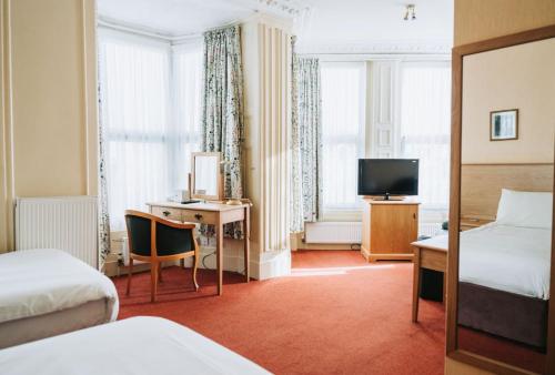 um quarto de hotel com uma cama, uma secretária e uma televisão em Welbeck Hotel & Apartments em Douglas