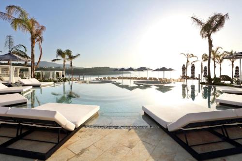 a swimming pool with lounge chairs and palm trees at BLESS Hotel Ibiza - The Leading Hotels of The World in Es Cana