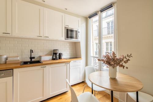une cuisine avec des placards blancs et une table avec un vase de fleurs dans l'établissement Modern spacious studio only 1 minute away from the Place de la République, à Paris