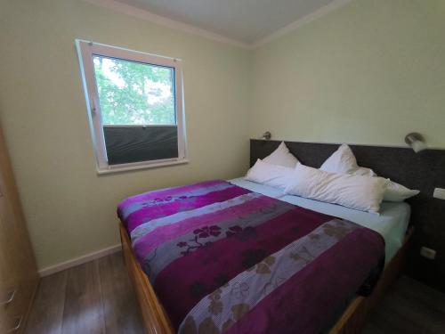 um quarto com uma cama com um edredão roxo e uma janela em Ferienhaus Am Dünenwald em Glowe