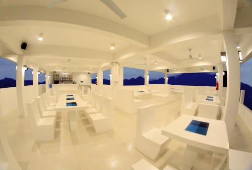 Habitación blanca con mesas blancas y bancos blancos en Bluewave Hotel en Corón