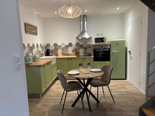une cuisine avec des armoires vertes, une table et des chaises dans l'établissement Gîte à 10 min de Dinan avec bain nordique privatif, à Corseul
