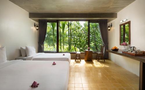 a bedroom with two beds and a large window at The Nature & Villas in Siem Reap