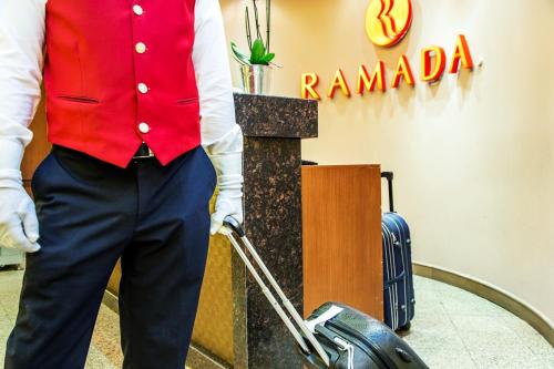 a man in a red shirt and trousers with a suitcase at Ramada by Wyndham Sofia City Center in Sofia