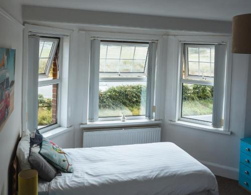 a bedroom with three windows and a bed in it at Sea Jade Guest House in Bude