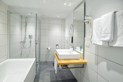 a white bathroom with a sink and a shower at Tulip Inn Ludwigshafen City in Ludwigshafen am Rhein