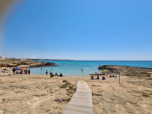 a wooden path on a beach with people in the water at casa al mare kalispera in Marina di Mancaversa