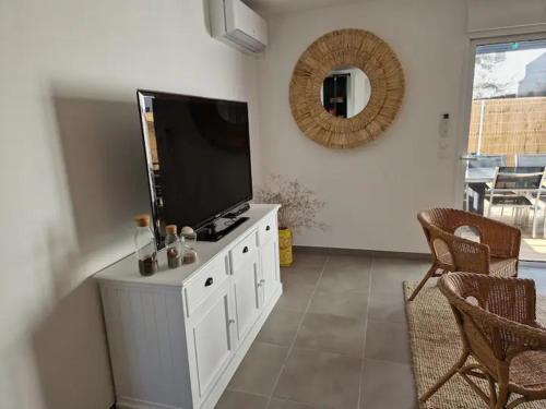 salon z telewizorem z płaskim ekranem na białej szafce w obiekcie Maison neuve clim 400m plage w Saintes-Maries-de-la-Mer