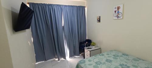 a bedroom with a window with blue curtains at Alojamiento Acogedor in San Felipe de Puerto Plata