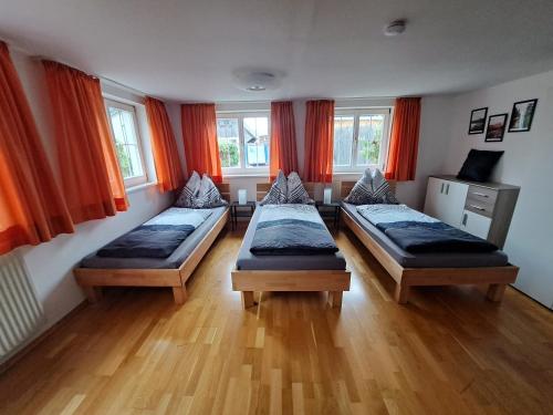 three beds in a room with orange curtains at ZADRA Home in Dornbirn