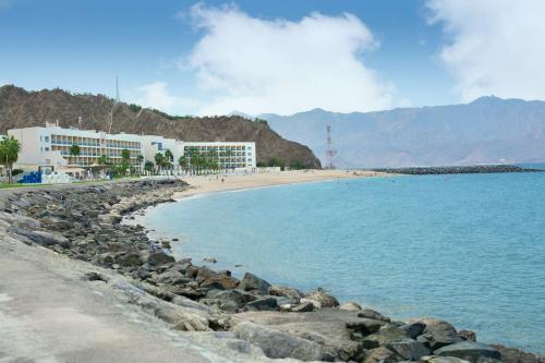 a beach with a building and a beach with rocks at Radisson Blu Resort, Fujairah in Dibba