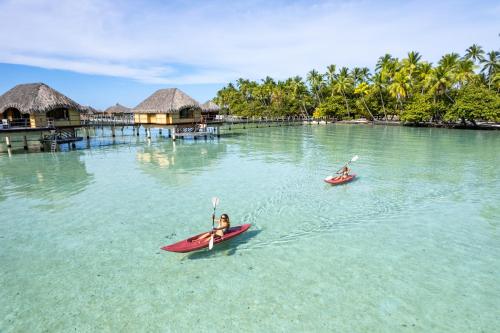 two people in kayaks in the water near a resort at Le Taha'a by Pearl Resorts in Motu Tautau