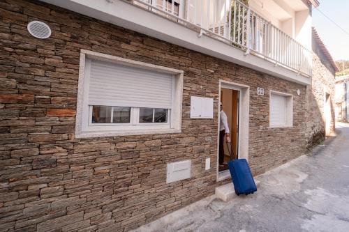 a man standing outside of a brick building with a blue suitcase at Houses São Pedro in São João da Pesqueira