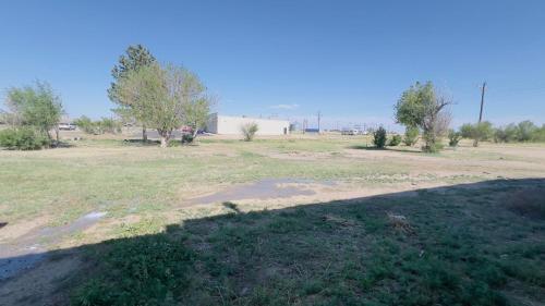 an empty field with trees and a building in the background at RV Sites For Rent -Power-Water-Sewer-Wifi in Eads