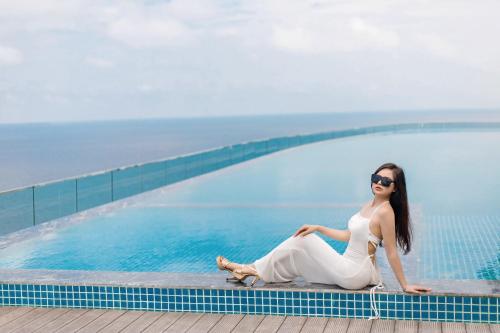 a woman in a white dress sitting next to a swimming pool at Flamingo Hai Tien in Hoằng Hóa