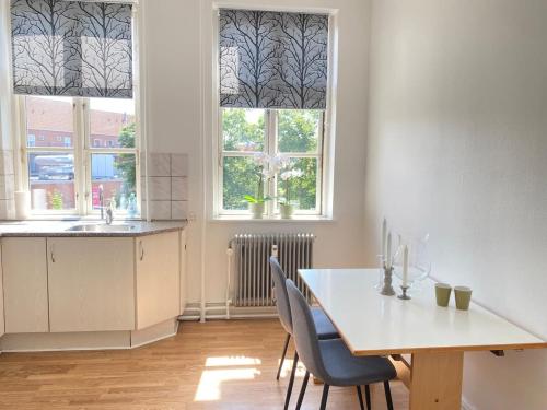 a kitchen with a table and chairs and two windows at Boutique lejlighed Nakskov in Nakskov