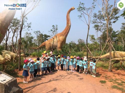 a group of children standing in front of a dinosaur at Novaworld Phan Thiết-7Days mart in Phan Thiet