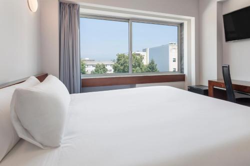 a bedroom with a large white bed and a large window at B&B HOTEL e Apartamentos Felgueiras in Felgueiras
