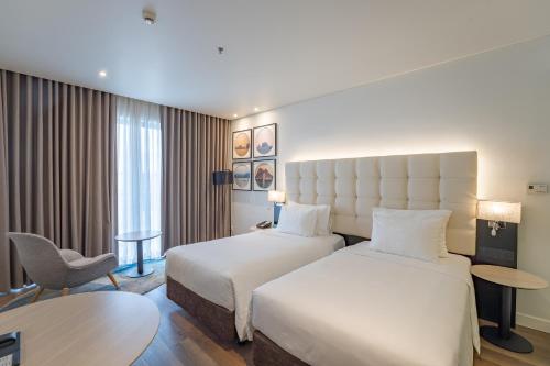 a hotel room with two beds and a chair at Hotel Soleil Ha Long, Trademark Collection by Wyndham in Ha Long