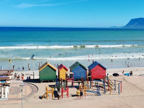 a beach with colorful beach huts and people in the ocean at Beach Hut Empire Apartment in Muizenberg