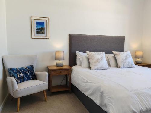 a bedroom with a white bed and a chair at Courtside Views Empire Apartment in Muizenberg