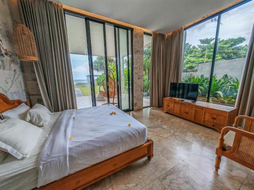 a bedroom with a bed and a tv and large windows at Ketewel Beach Villas and Spa in Ketewel