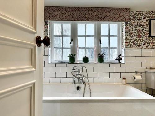uma banheira branca na casa de banho com 2 janelas em Worlington Hall em Worlington
