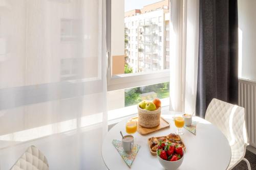 a white table with a bowl of fruit and a window at Nemea Appart Hotel Grand Cœur Nancy Centre in Nancy