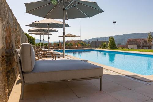 a lounge chair with an umbrella next to a swimming pool at Hotel Rural Quinta de Sao Sebastiao in Barroselas