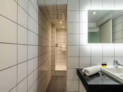 uma casa de banho em azulejos brancos com um lavatório e um espelho. em Mercure Bedford Centre Hotel em Bedford