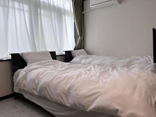 2 Betten in einem Schlafzimmer mit weißer Bettwäsche und einem Fenster in der Unterkunft The Guest House Noah in Naha
