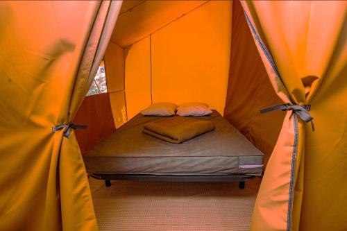 un petit lit dans une tente avec deux rideaux dans l'établissement Camping Onlycamp Les Berges de l'Yonne, à Coulanges-sur-Yonne