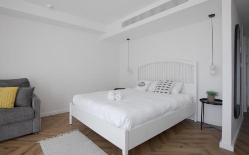 a white bedroom with a white bed and a couch at סוויטות עם נוף צמודות לים במתחם SeaSide היוקרתי עם בריכה - By SEAELO EILAT in Eilat