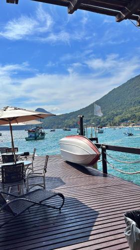 a wooden deck with chairs and an umbrella and a boat at Pousada Convés - Ilha Grande in Praia de Araçatiba
