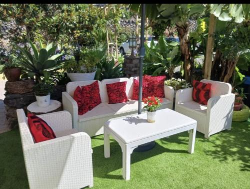 a patio with white chairs and a table with red pillows at Hotel Rural La Raya 1866 in Güimar