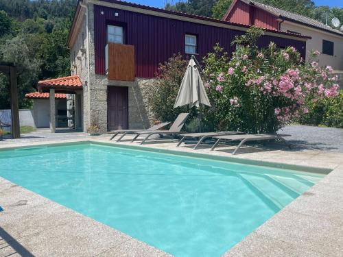 a swimming pool with two chairs and an umbrella at Refúgio do Abade in Terras de Bouro