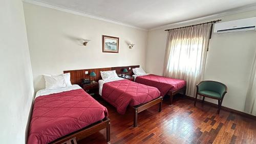 a hotel room with two beds and a chair at Hotel Trindade Coelho in Mogadouro