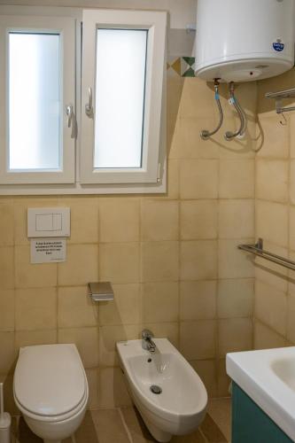 a bathroom with a toilet and a sink and two windows at Seasons Home San Foca in San Foca