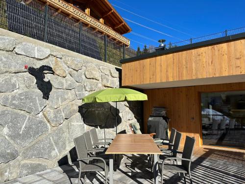 a wooden table with a green umbrella next to a stone wall at Exklusives Chalet-Haus mit Gletscherblick in Neukirchen am Großvenediger