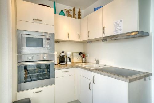 eine Küche mit weißen Schränken, einer Mikrowelle und einer Spüle in der Unterkunft Ferienpark - Haus H, App 0H0501 in Heiligenhafen