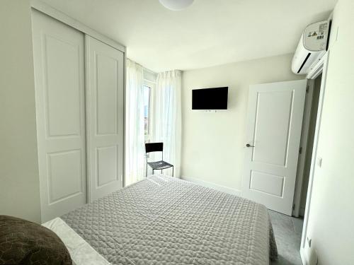 a white bedroom with a bed and a television at Apartamento Calas in Noja
