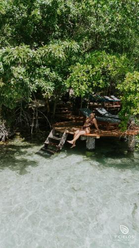a woman sitting on a bench next to a body of water at 7 CIELOS BACALAR. in Bacalar