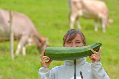 a woman holding a zucchini in a field with cows at Sonnmatt Bergpension & Gesundheitszentrum in Ebnat