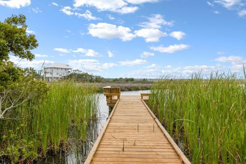 a wooden dock in a marsh with a house in the background at Palm Beach North in North Topsail Beach