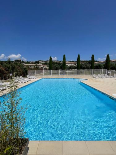 une grande piscine bleue avec des chaises et des arbres dans l'établissement Appartement Climatisé Terrasse et Piscine Le Baptistou, à Paradou